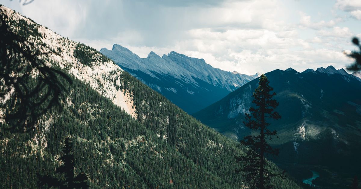 Stunning landscape of Banff's rocky mountains with lush forests under a cloudy sky.